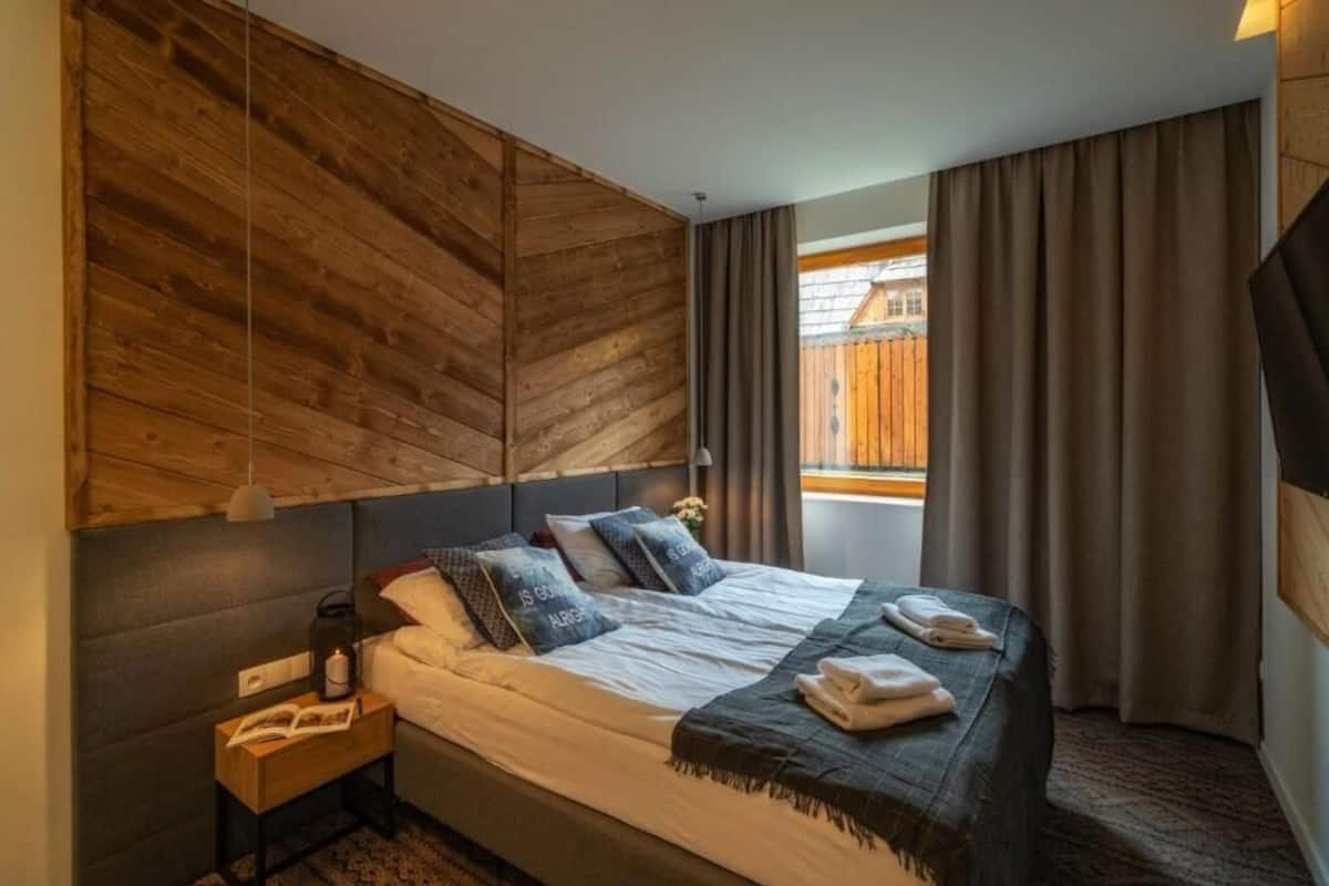 A hotel room with a bed, a nightstand, a lamp, a window with curtains, and a view of the outside.