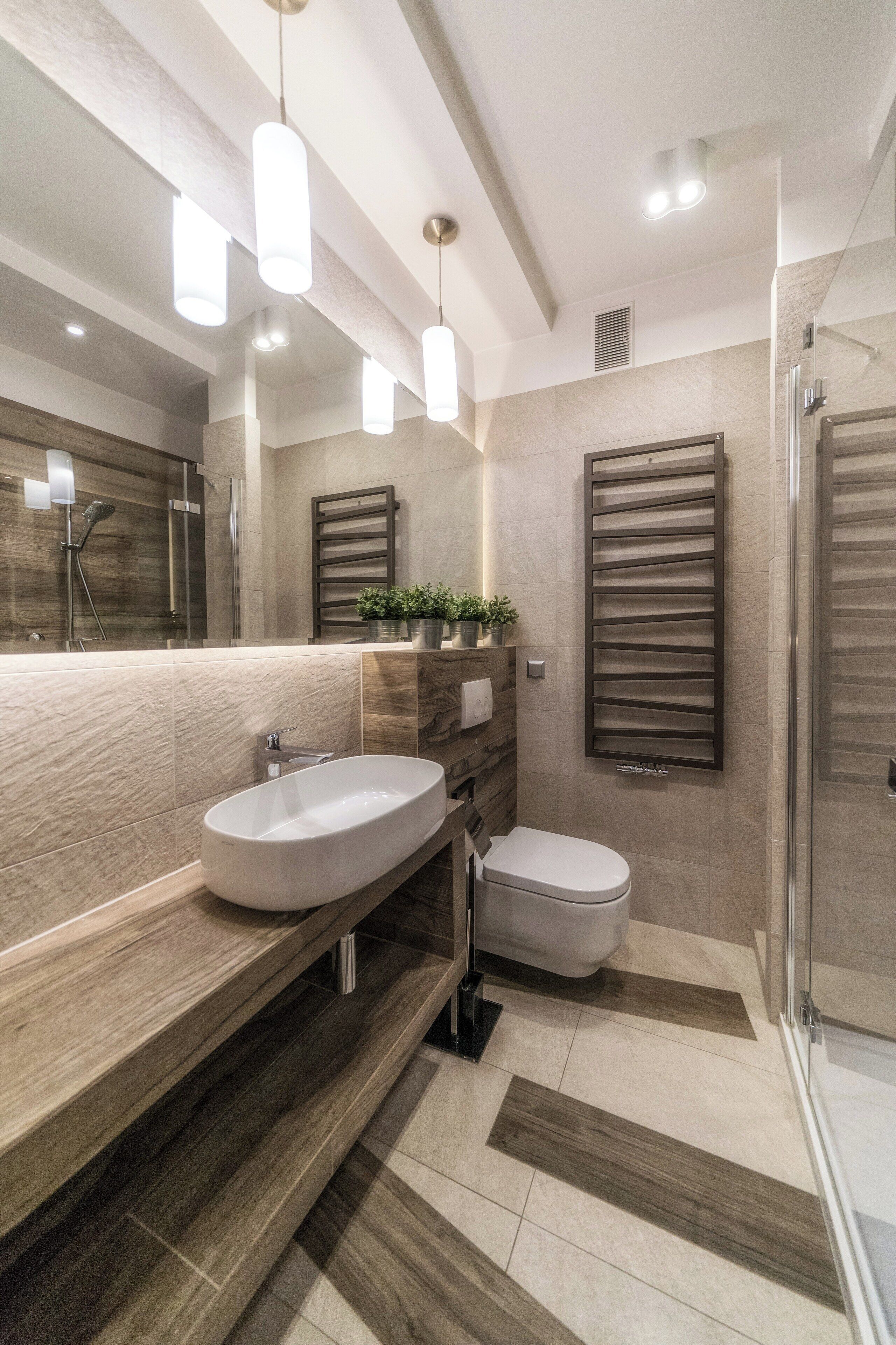 A modern bathroom with a large mirror, a sink, and a toilet. There are wooden shelves and a potted plant.
