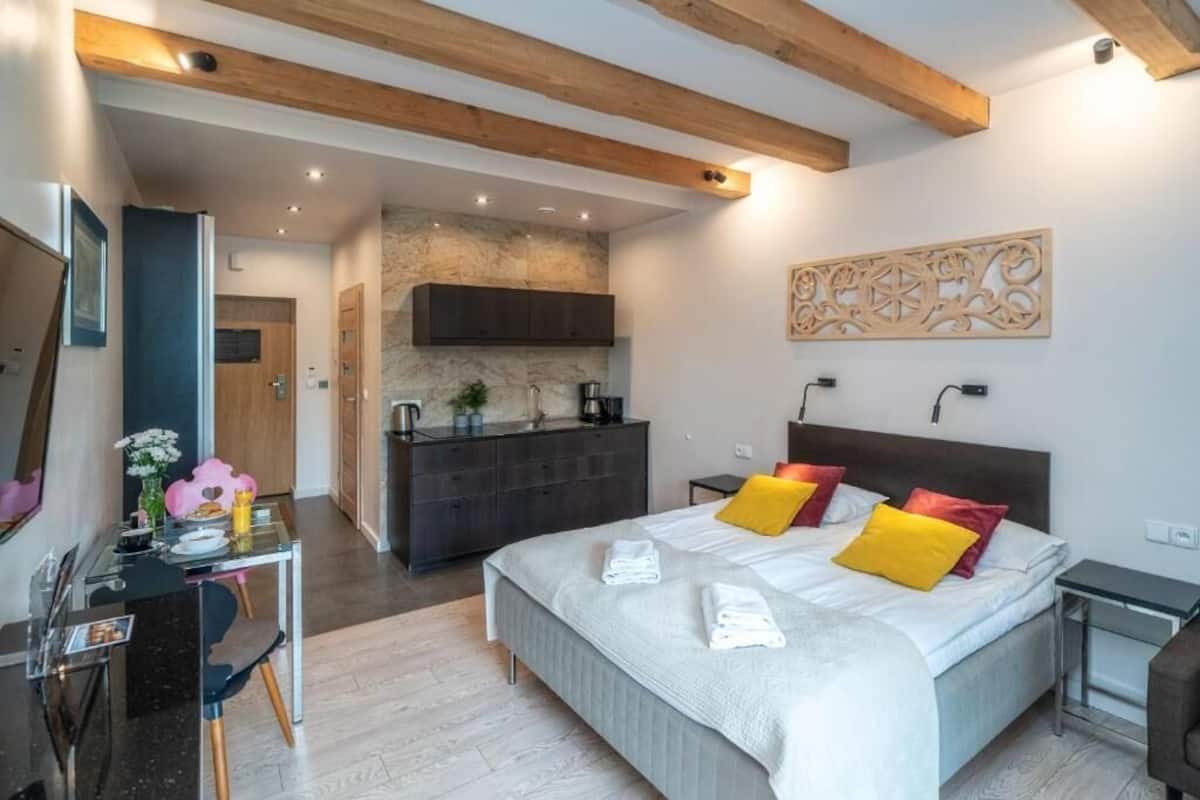 A modern hotel room with a large bed, a desk, and a kitchenette.