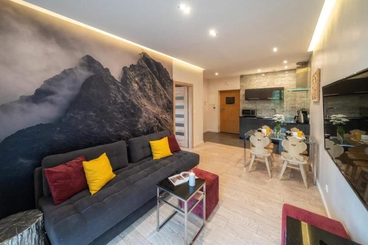 A modern living room with a sofa, a dining table with chairs, and a kitchen area in the background.