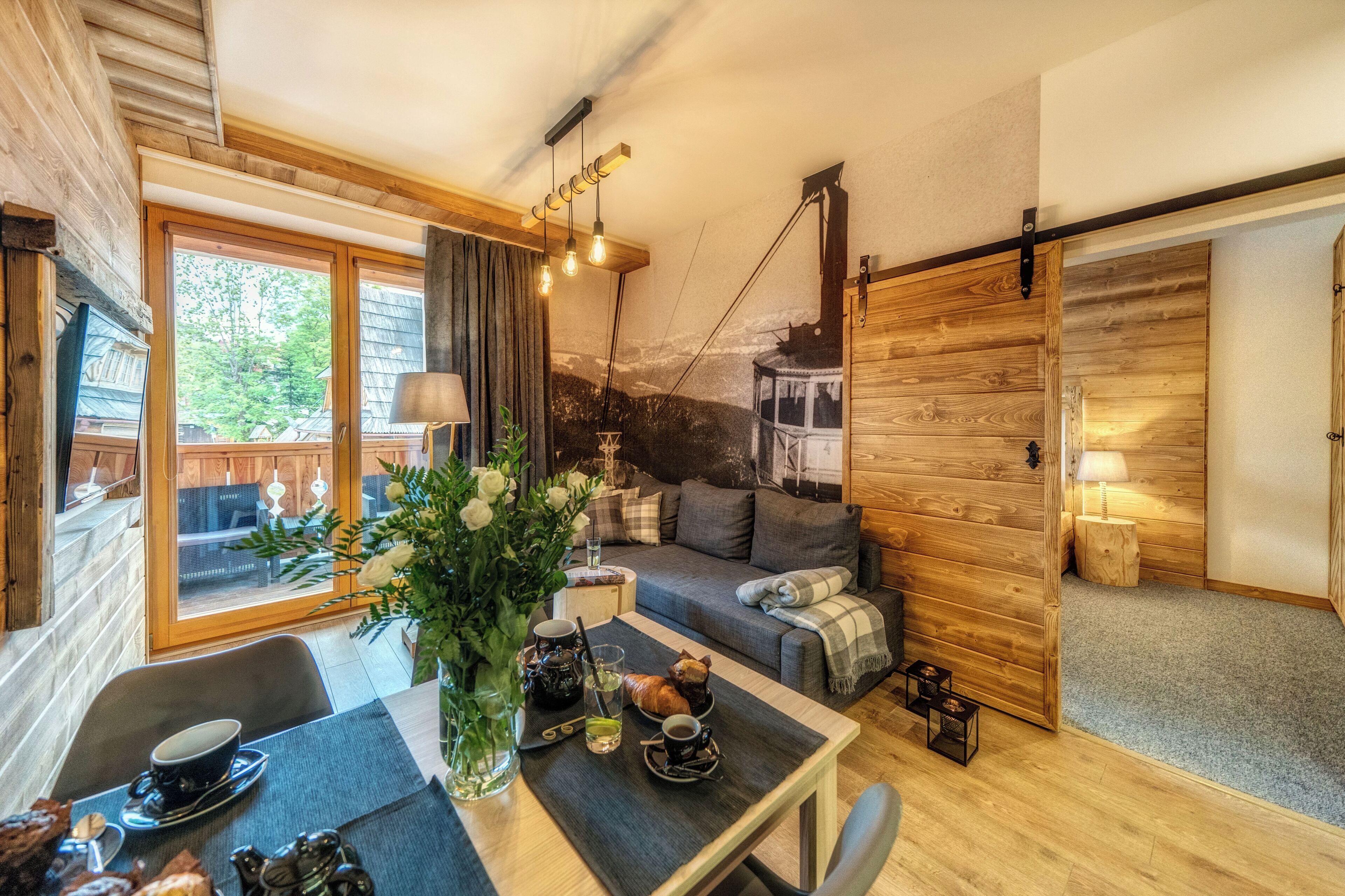 A cozy room with a wooden interior, a dining table with a vase of flowers, a sofa, and a sliding door.