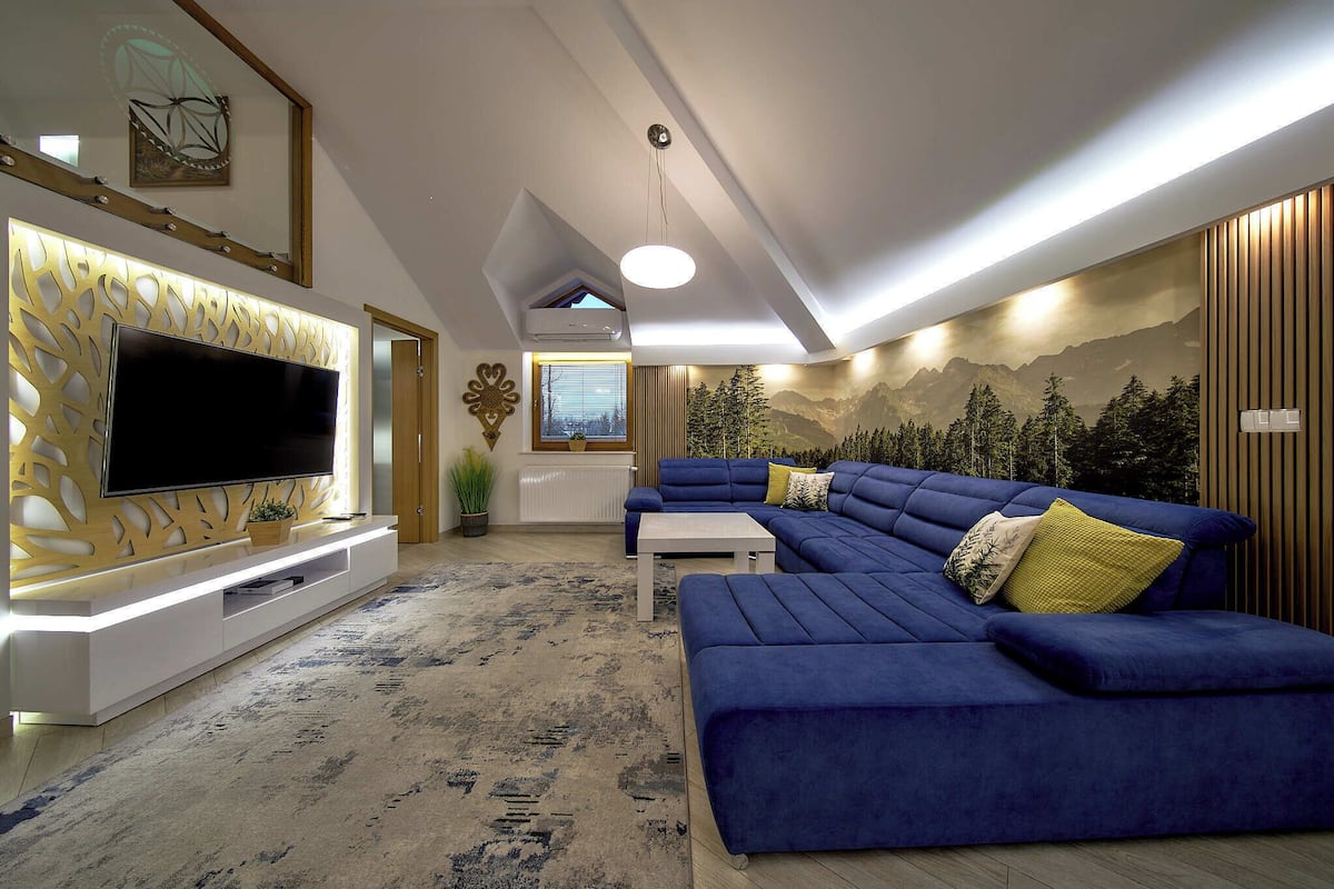 A modern living room with a sectional sofa, a flat-screen TV, and a decorative wall panel.