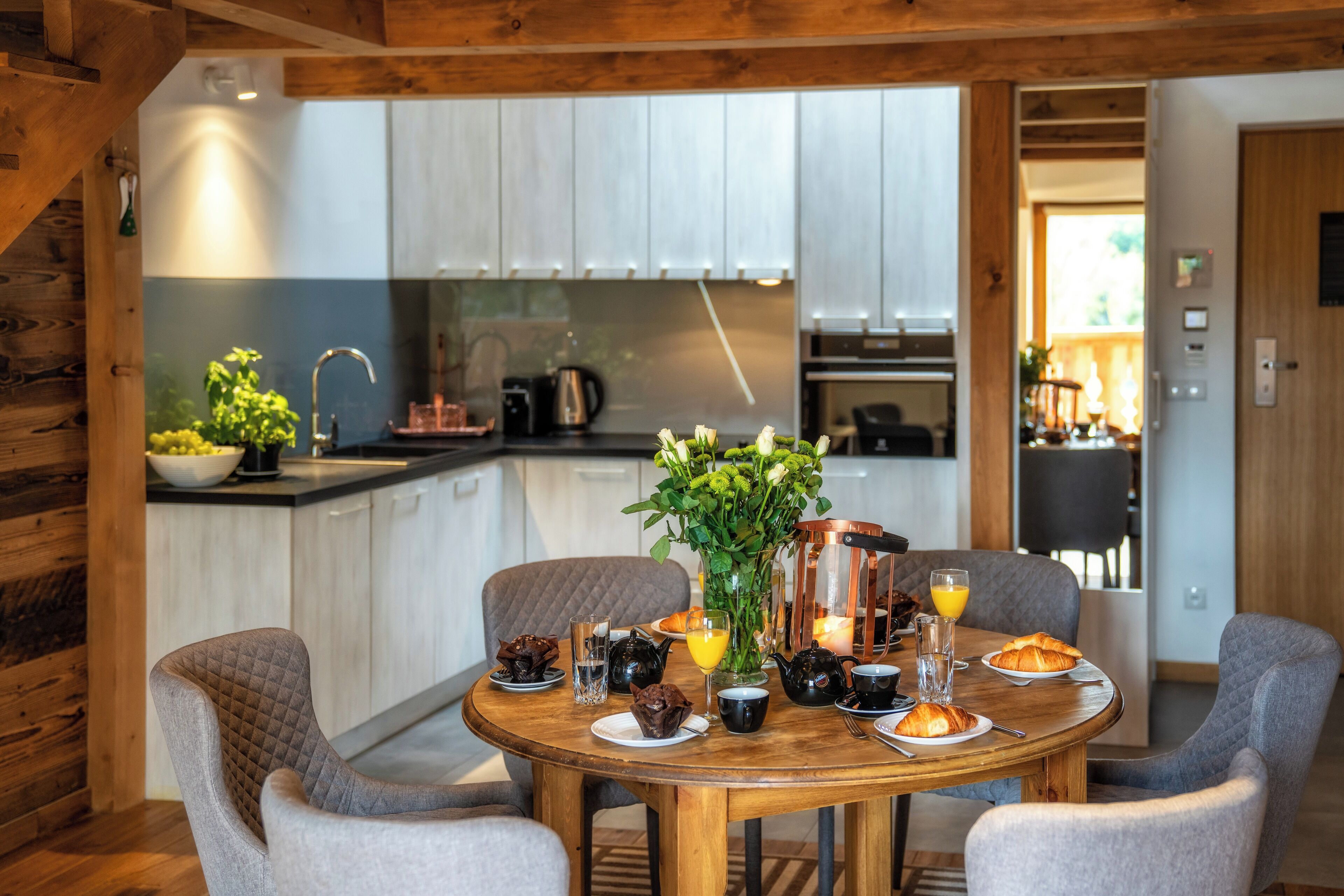 A wooden dining table with chairs, a vase of flowers, and breakfast items.