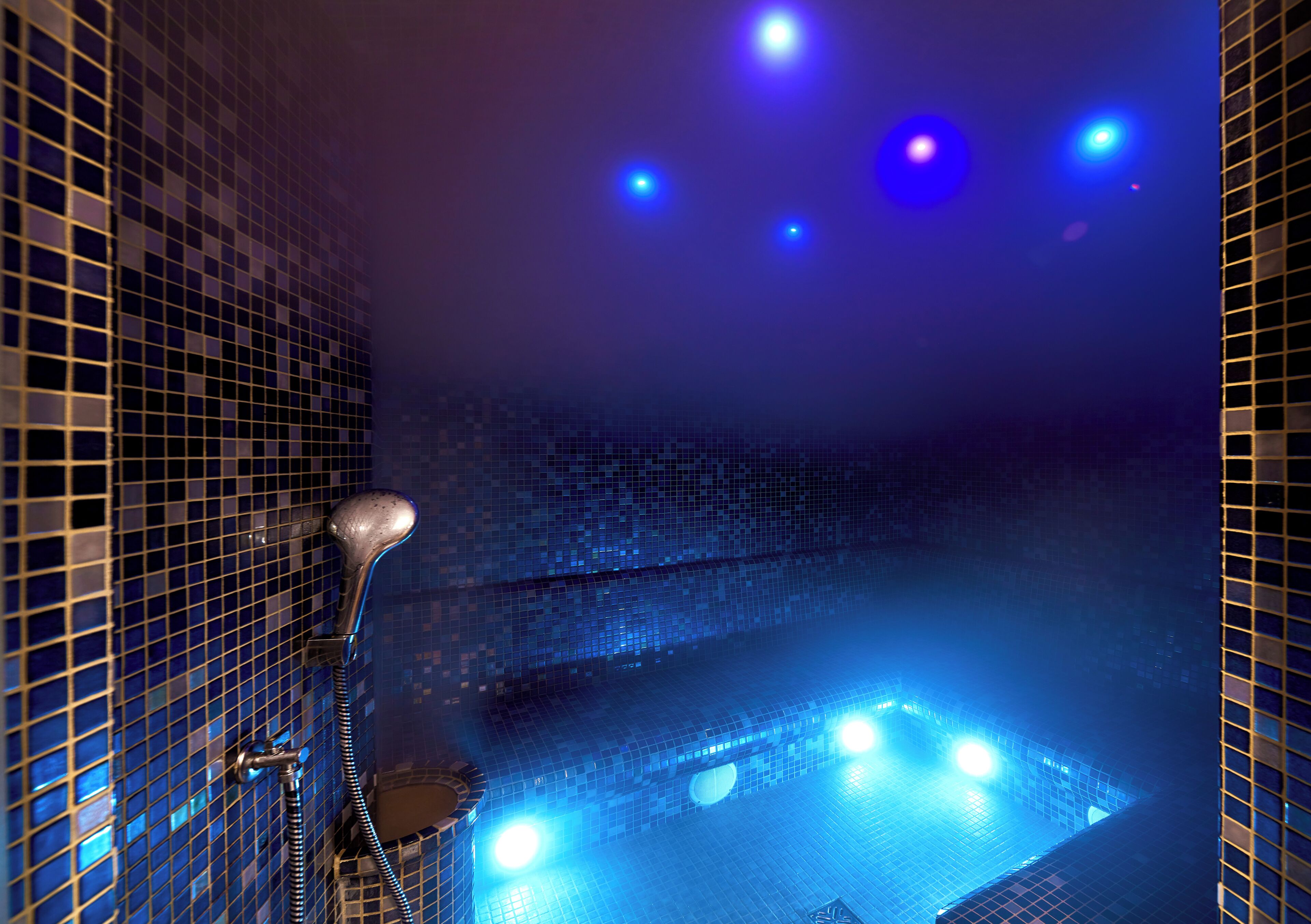 Une salle de bain avec un sol carrelé, un espace douche et une baignoire dotée d’un éclairage bleu.