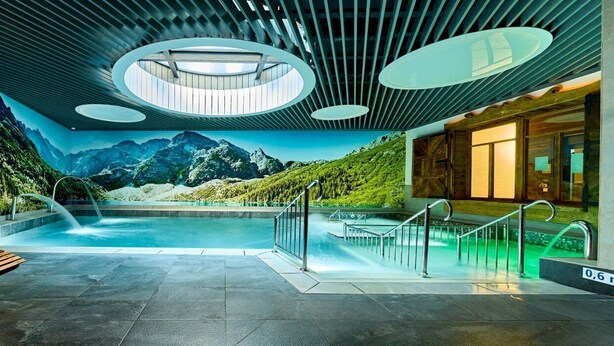 Un área de piscina interior moderna con un mural de montañas, bancos de madera y barandilla de vidrio.