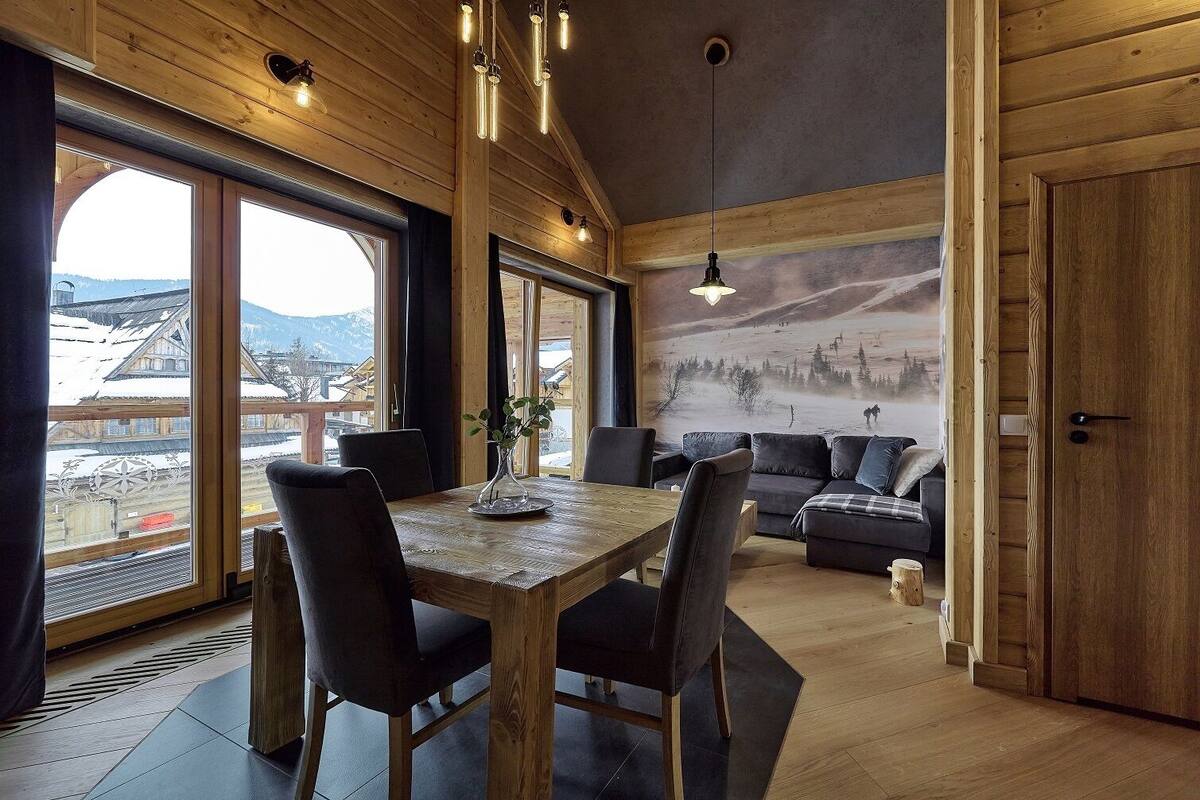 A wooden interior with a dining table, chairs, a sofa, and a mural of a snowy landscape.