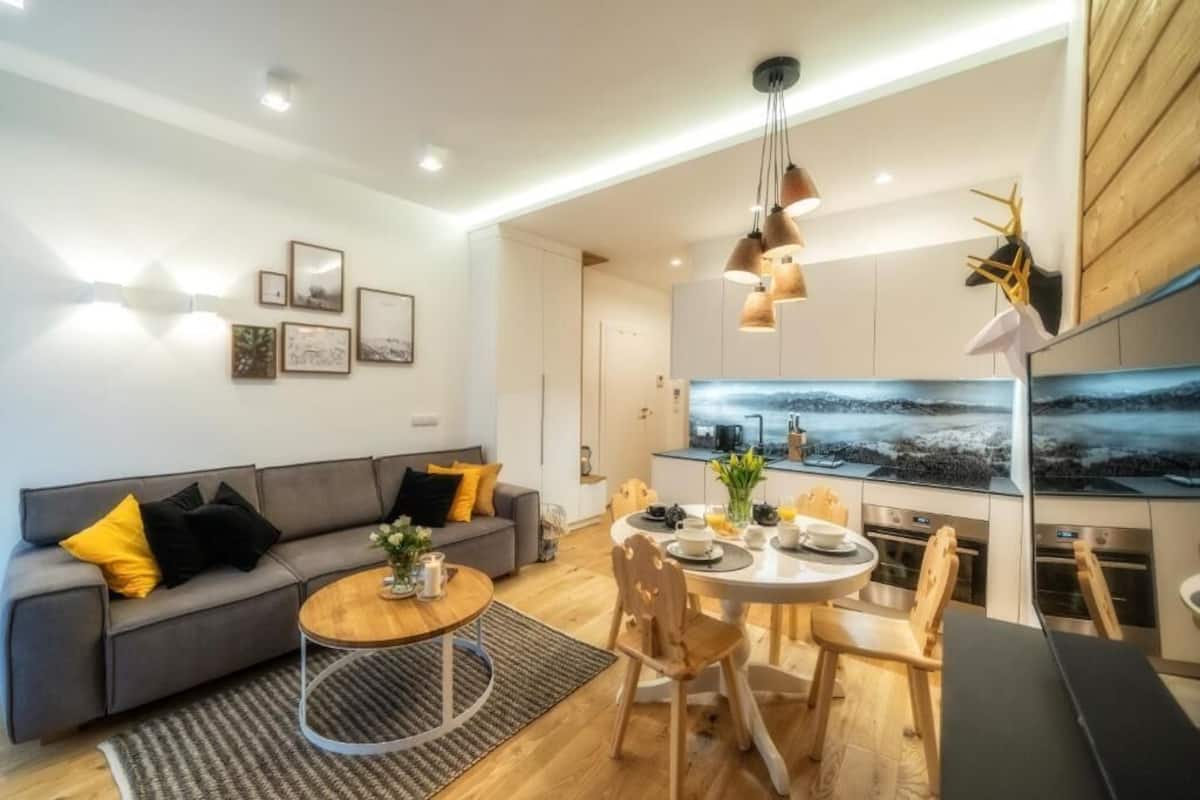 A modern living room with a grey sofa, a round wooden coffee table, and a dining area with a white table and chairs.
