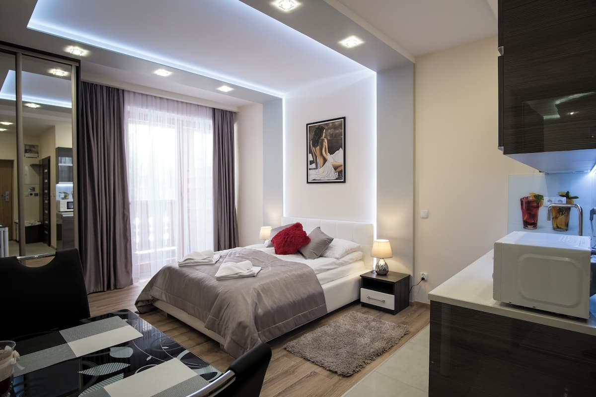 A modern hotel room with a bed, bedside table, lamp, and a microwave.