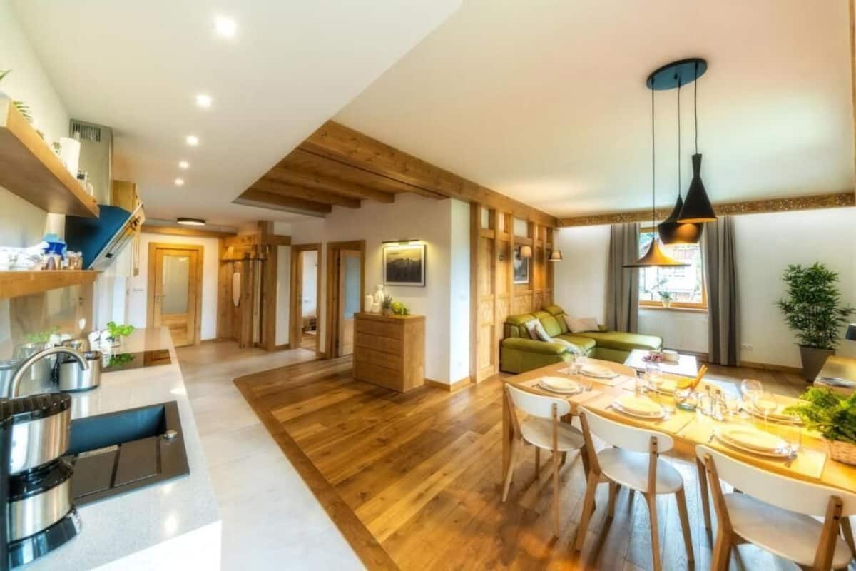A modern kitchen with wooden beams, a dining area with a table set for four, and a cozy living space with a green sofa.