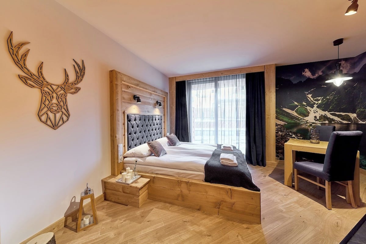 A modern bedroom with a large bed, a wooden headboard, a desk with a chair, and a mural on the wall.