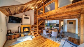 Interior acogedor de una cabaña con chimenea, escalera de madera, comedor y cocina.