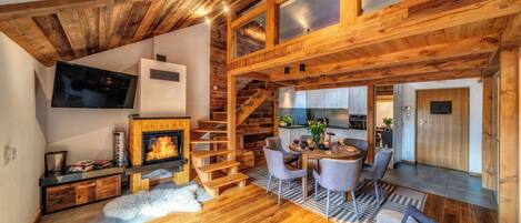 A cozy cabin interior with a fireplace, wooden staircase, dining area, and kitchen.