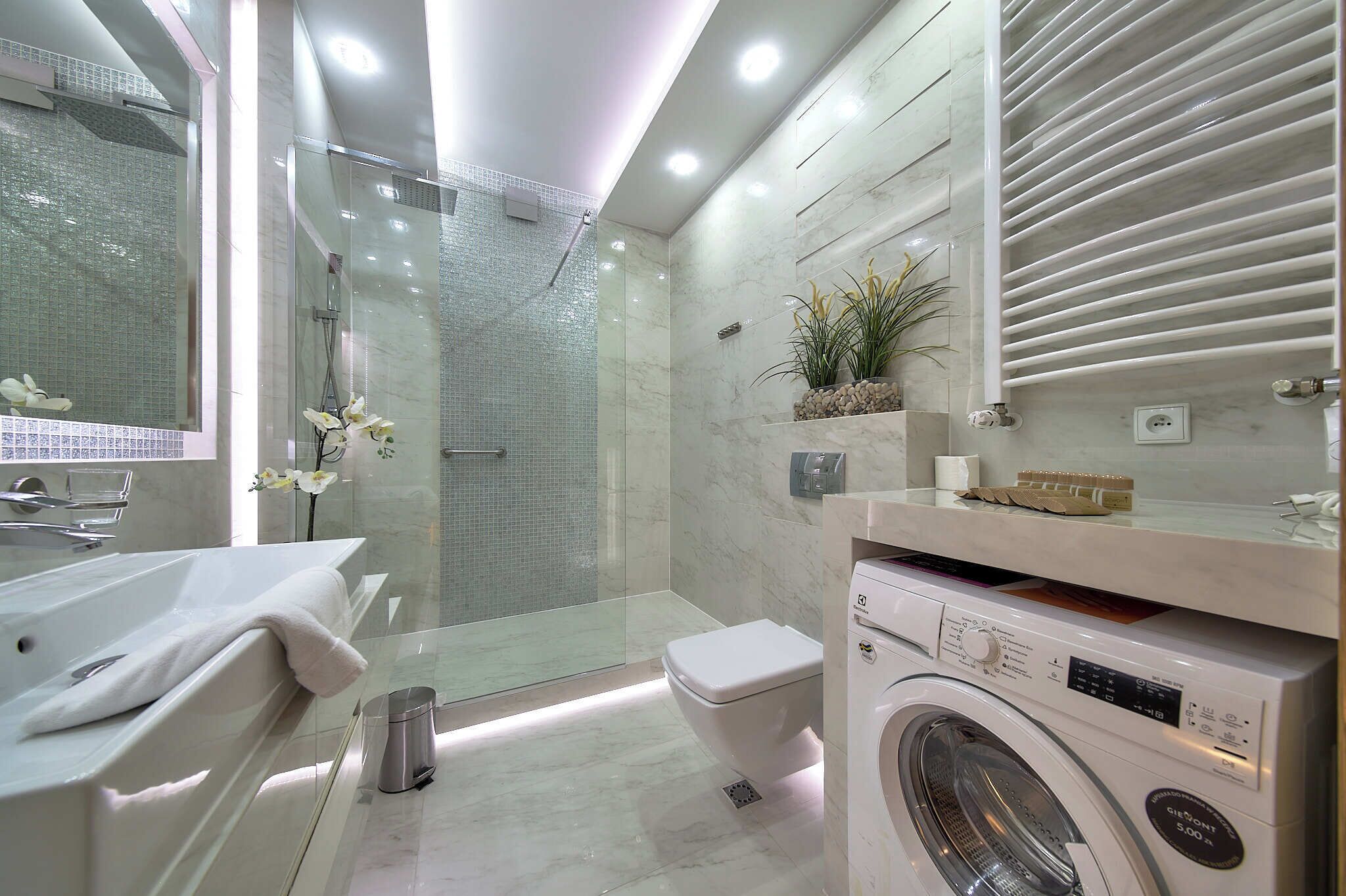 Un baño moderno con ducha de vidrio, bañera blanca, inodoro y lavadora integrada.