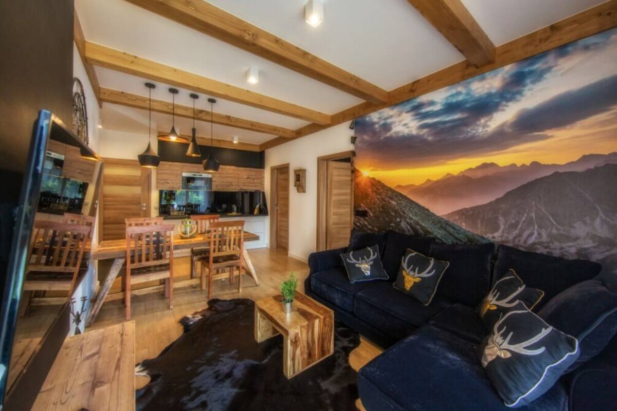 A modern living room with a large sofa, wooden dining table, and a kitchen in the background.