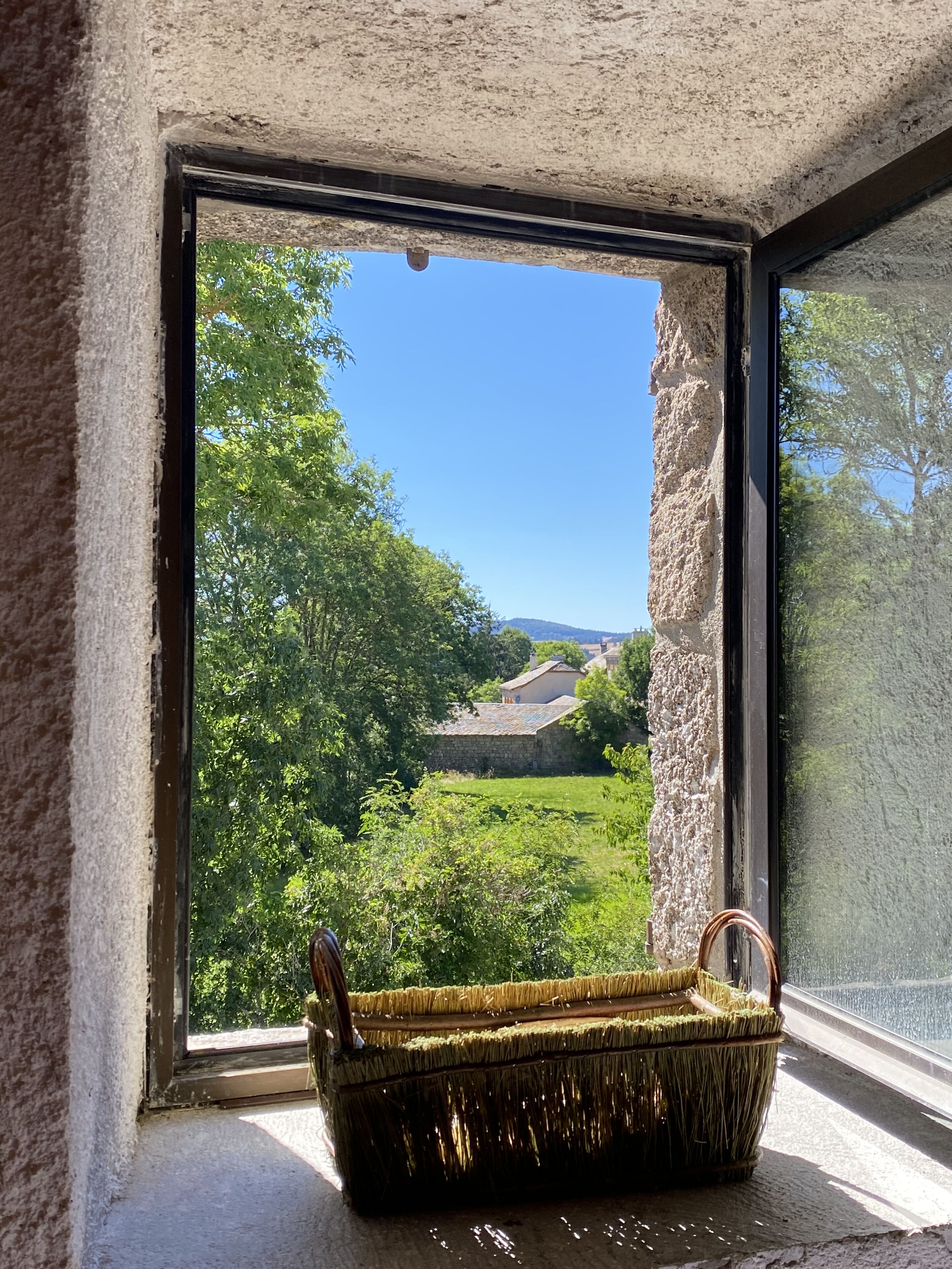 A window with a view of a green landscape and a stone wall.