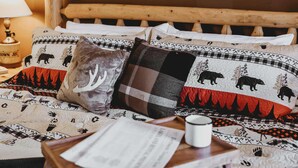 Una cama con cabecera de madera, varios almohadones con estampados de animales, una mesita de noche con una lámpara y una taza.