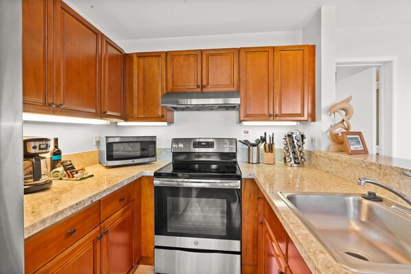 A kitchen with wooden cabinets, a stainless steel oven, a microwave, and a sink. - 1 Br Ocean View Getaway at Pali Ke Kua 108 (Princeville)