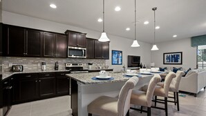 A modern kitchen with dark cabinets, a large island with bar stools, and pendant lighting. - PROMO Magical 10 BR Villa, Pool/Spa, Resort - by Blue Sky Villas (Kissimmee)