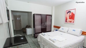 Quarto de hotel com cama, escrivaninha, cadeira, guarda-roupa e um quadro na parede.