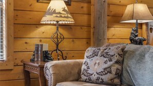 Une pièce chaleureuse avec des murs en bois, un canapé confortable, une table avec une lampe et une statue d’ours décorative.