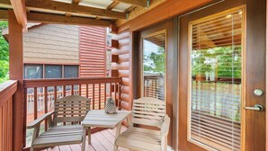 Una terraza de madera con dos sillas y una mesa, una puerta corrediza de vidrio y vista a follaje.