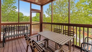 Une terrasse en bois avec une table et des bancs, de grandes fenêtres et un ventilateur de plafond.