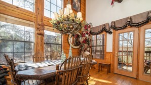 A wooden dining area with a chandelier, rustic chairs, and large windows.