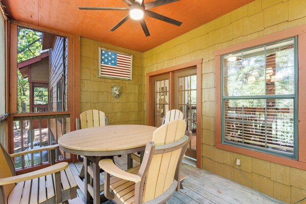 A wooden deck with a round table and chairs, an American flag, and a ceiling fan. - Walk-in Cedar Log Cabin with Gas Fireplace & Whirlpool Tub Show Ticket and Golf Discounts! (Branson)