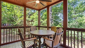 A wooden deck with a round table and chairs, surrounded by a wooden railing, overlooking a forested area.