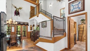 A spacious interior with a wooden staircase, a dining area with a chandelier, and a mounted deer head.