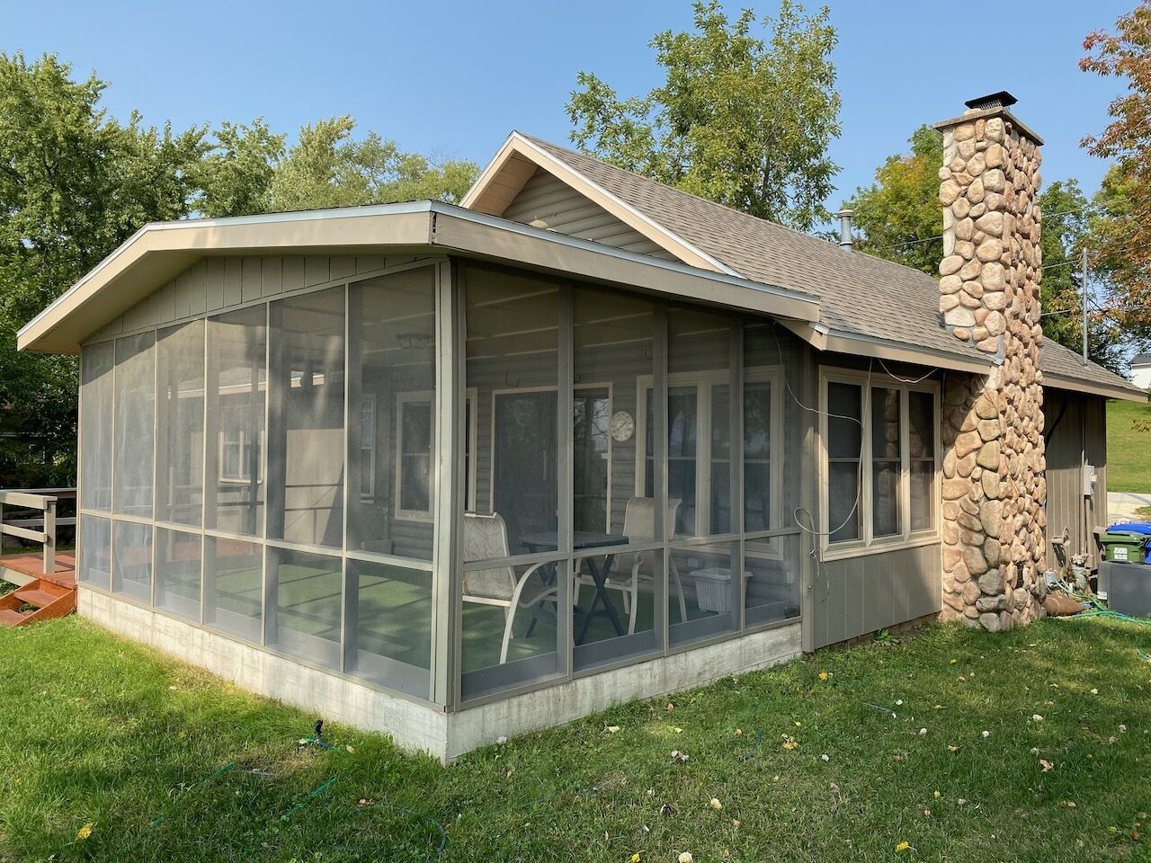 A covered patio with a stone chimney, a glass enclosure, and outdoor seating.
