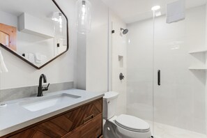 A modern bathroom with a white sink, dark wooden vanity, a toilet, and a glass-enclosed shower area. - Sunsets in Copper Mountain CO:- Ski in/Ski out with an amazing view (Frisco)