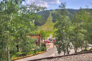 A view of a mountain road leading to a building with outdoor seating, surrounded by trees and a forested hillside. - Sunsets in Copper Mountain CO:- Ski in/Ski out with an amazing view (Frisco)