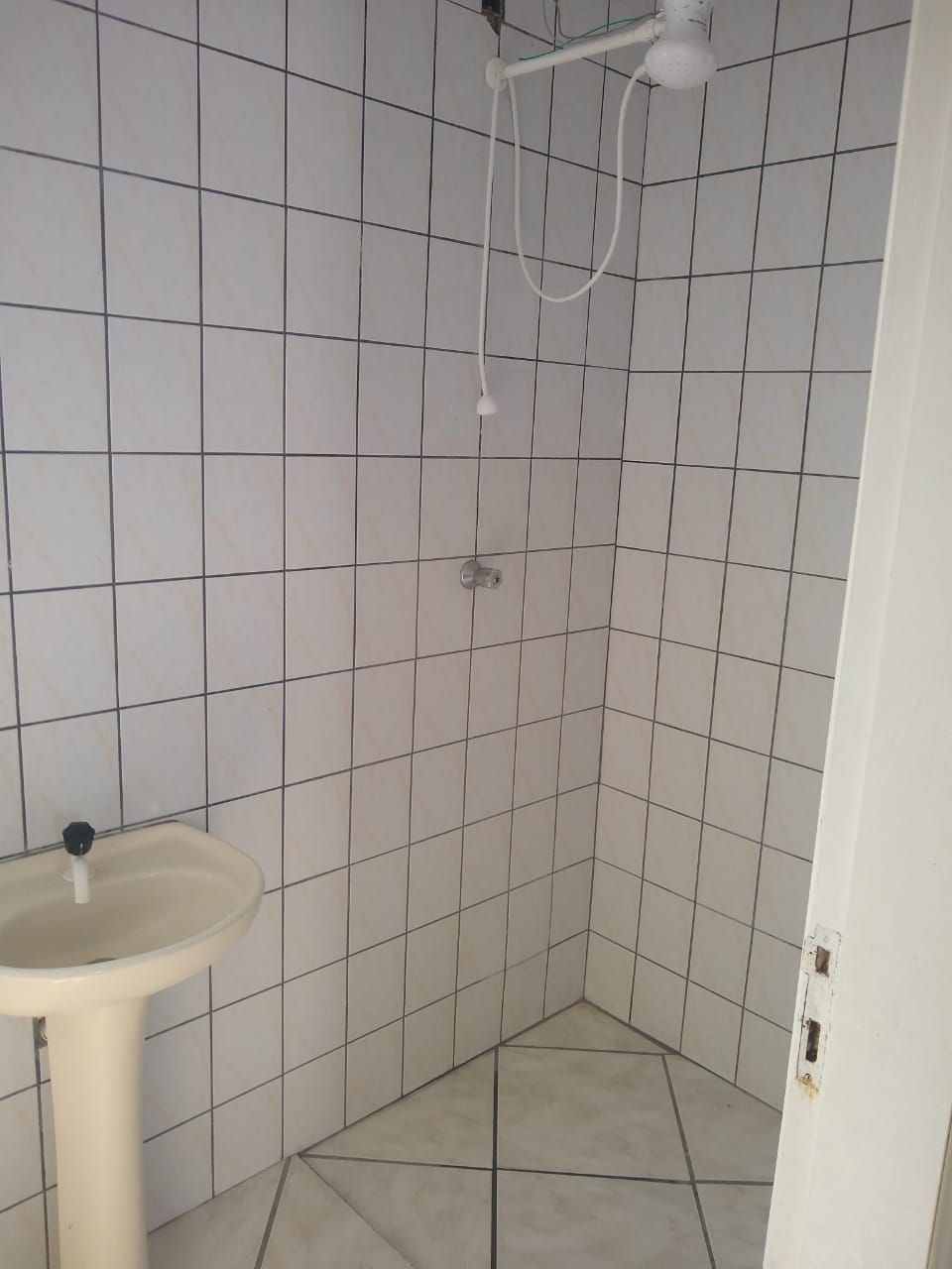 Casa de banho pequena com azulejos brancos, uma pia e um chuveiro.