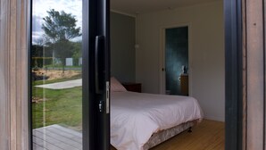 Ein Schlafzimmer mit einem Bett, Holzboden, einer Glastür, die nach draußen führt, und einem kleinen Nachttisch mit einer Lampe.