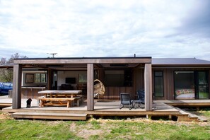 Ein modernes Haus mit überdachter Terrasse, Sitzgelegenheit im Freien und einem großen Fenster mit Blick auf den Garten.