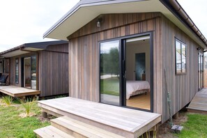 Eine moderne Holzblockhütte mit einer großen Glasschiebetür, die in ein Schlafzimmer mit Bett und Nachttisch führt.