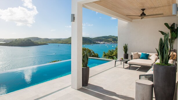 Un patio moderno al aire libre con piscina que da a una bahía pintoresca, un ventilador de techo y un mobiliario cómodo.
