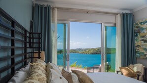 Un dormitorio con una cama grande, cabecera de madera y vistas a una masa de agua a través de puertas de vidrio.