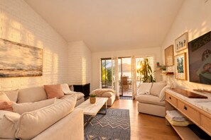 A spacious living room with a white brick wall, a fireplace, and a large window overlooking a garden.