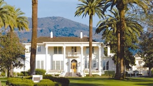 A large white building with a symmetrical facade, surrounded by palm trees and a mountain in the background.