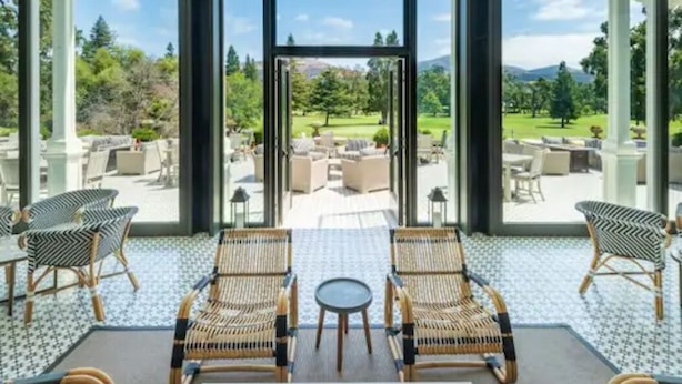 A spacious indoor area with large windows offering a view of an outdoor patio with furniture and greenery.