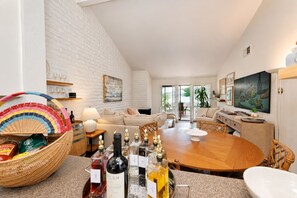 Una sala de estar moderna con una pared de ladrillo blanco, una mesa de comedor redonda de madera y un área de estar acogedora con sofás y sillones.