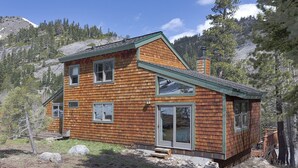 Une cabane en bois à deux étages, dotée d’un toit en pente, de grandes fenêtres et d’une cheminée.