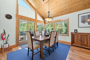 A dining area with a wooden table and chairs, large windows, a ceiling fan, and a fire extinguisher.