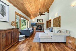 A spacious living room with a fireplace, wooden ceiling, and large windows.