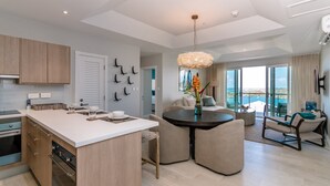 A modern kitchen with a central island, a dining area with a round table, and a living space with a view of the ocean. - Jade Stylish interior, Ocean Views, great amenities! (St. George)