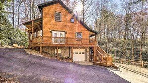 Una baita di legno a due piani con garage, un portico coperto e una scala che conduce al piano superiore.