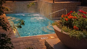 A hot tub with a waterfall feature, surrounded by a brick patio and a planter with colorful flowers. - Main Street | Walk to Shopping | Private Balcony (Park City)