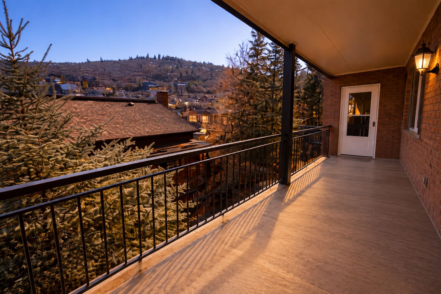 A balcony with a metal railing, a door, and a view of a town with buildings and trees.